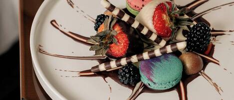 A dessert plate with various fruits and macarons on a white plate, placed on a wooden cabinet.