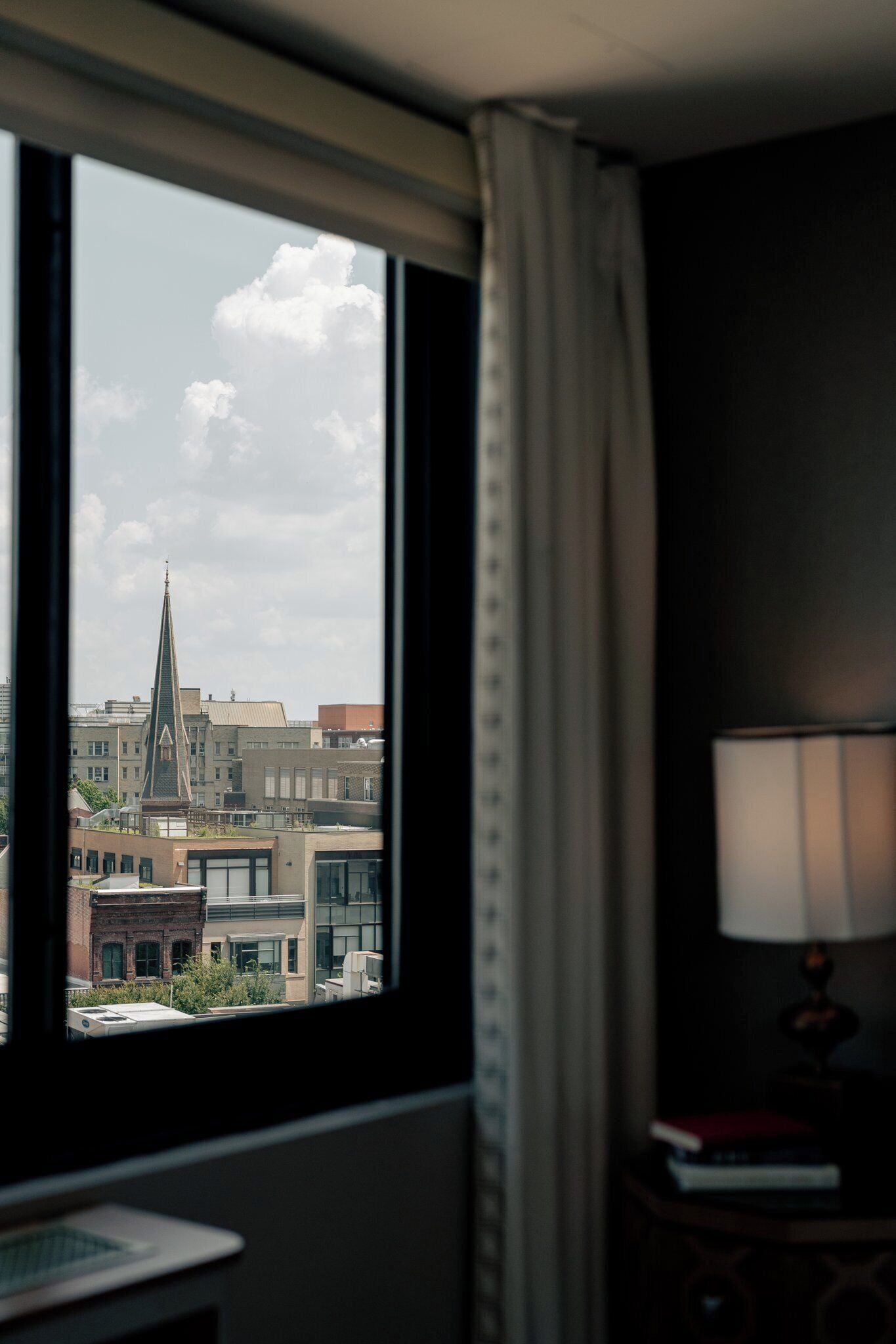 Habitación de hotel con un amplio ventanal que ofrece vistas a un paisaje urbano, incluyendo un edificio destacado con aguja.