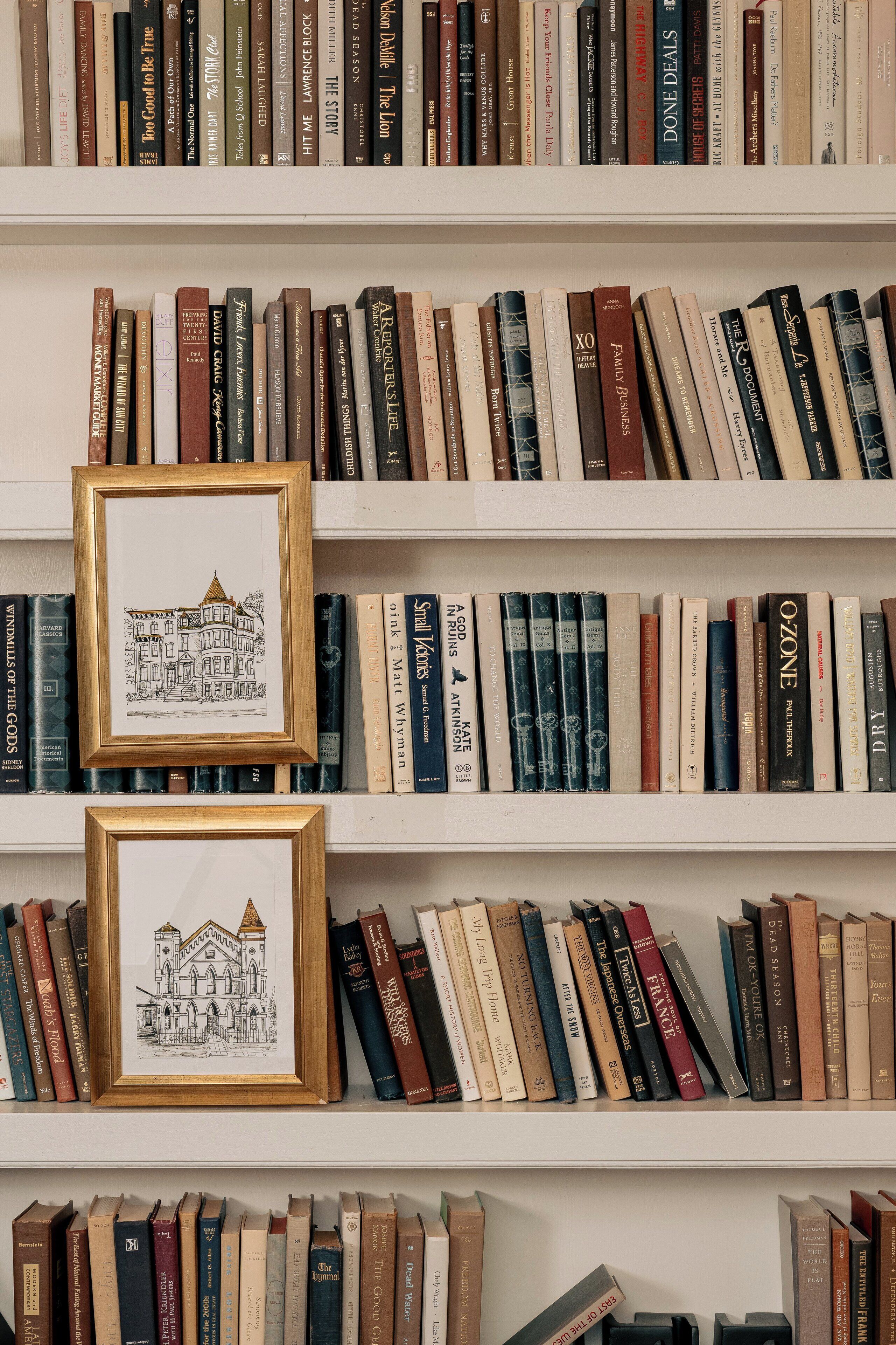 Ein Bücherregal voller Bücher und zwei gerahmte Illustrationen.