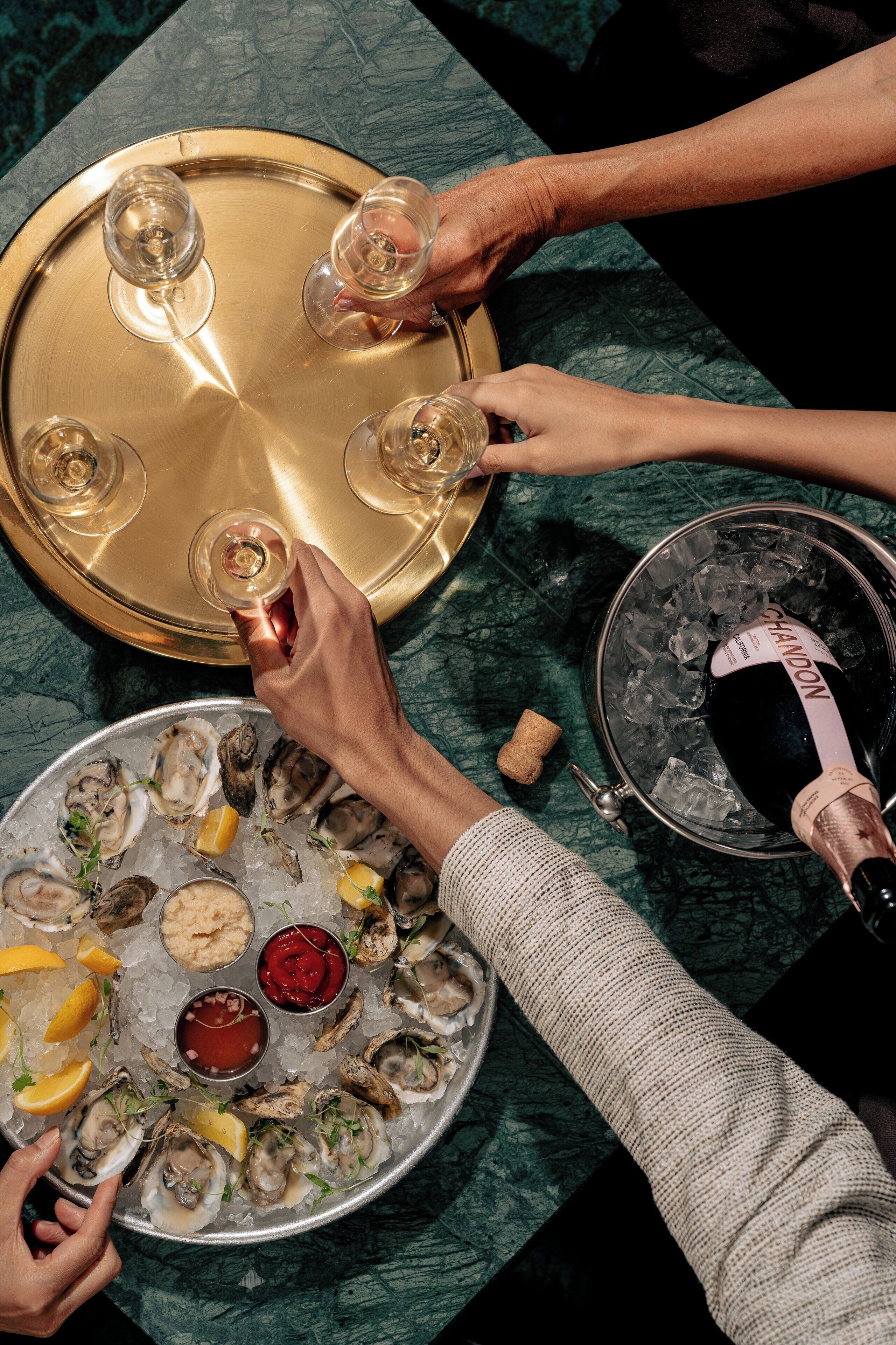 A table with oysters, lemon slices, and sauces, and a bottle of champagne being poured.