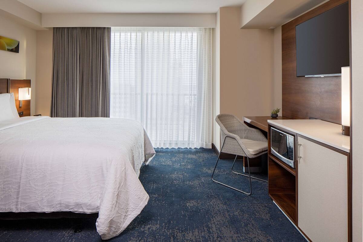 A hotel room with a large bed, a desk with a chair, a TV, and a window with curtains.