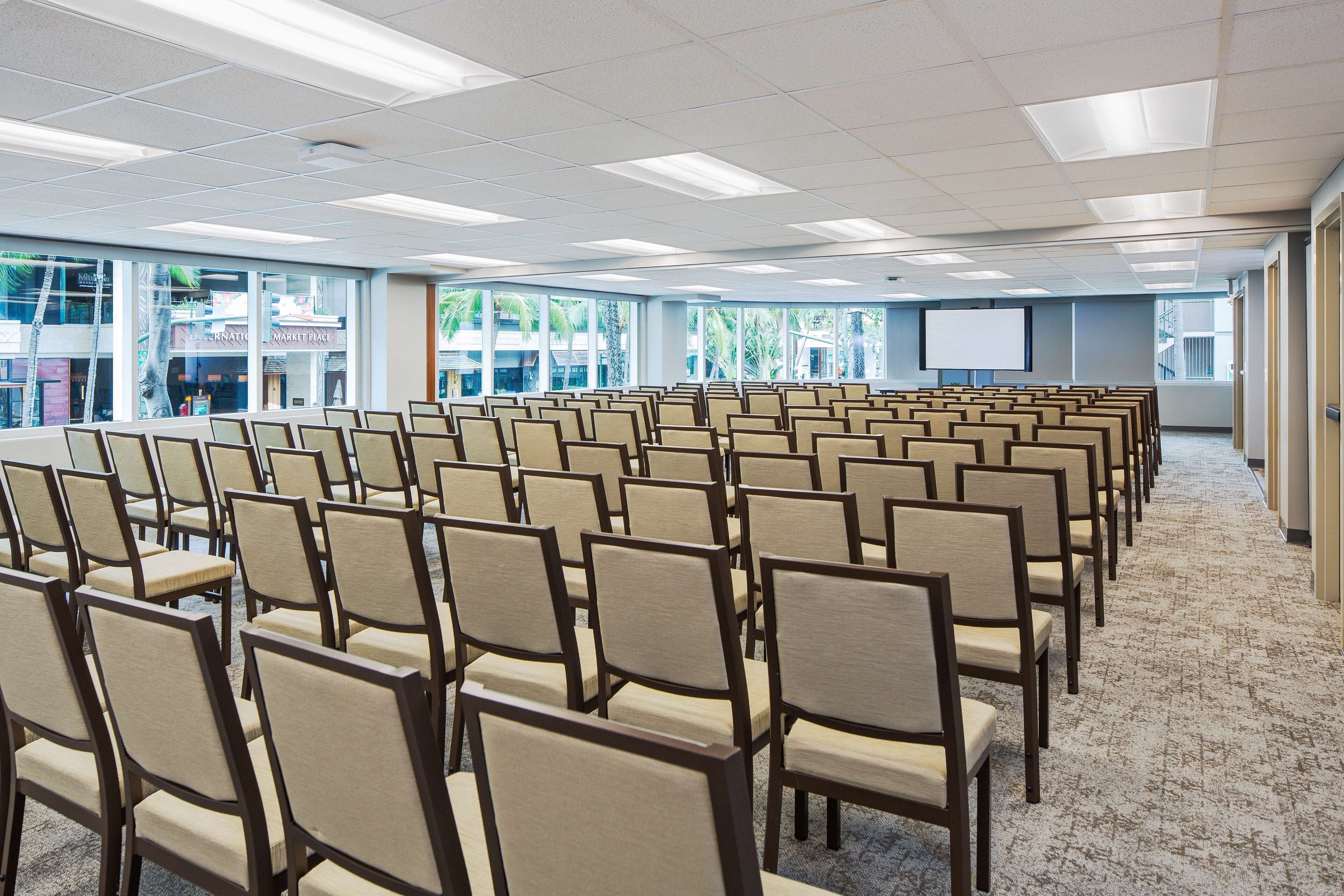 A conference room with rows of chairs, large windows, and a projection screen.