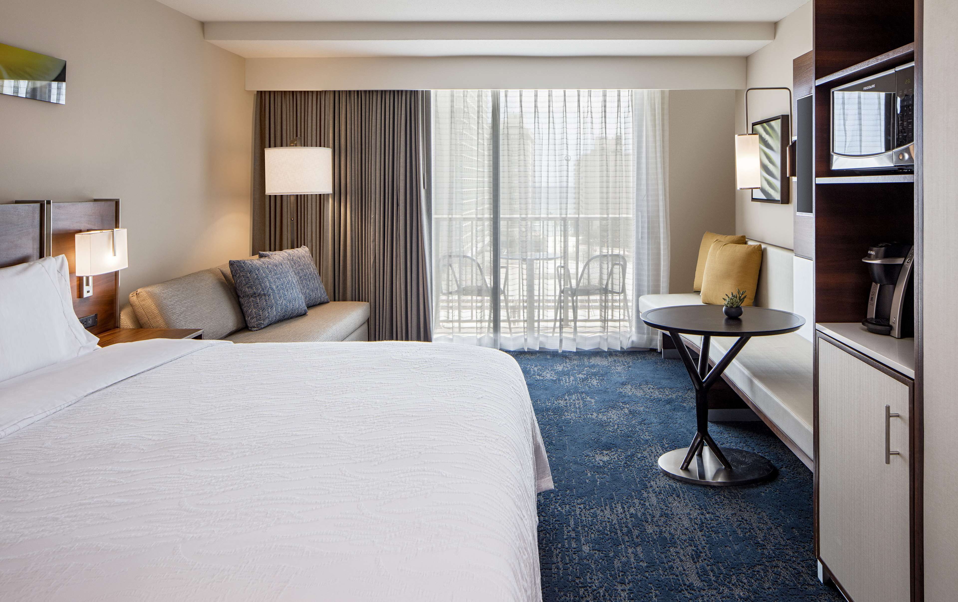 A hotel room with a large bed, a sofa, a small table, a TV, and a coffee machine.