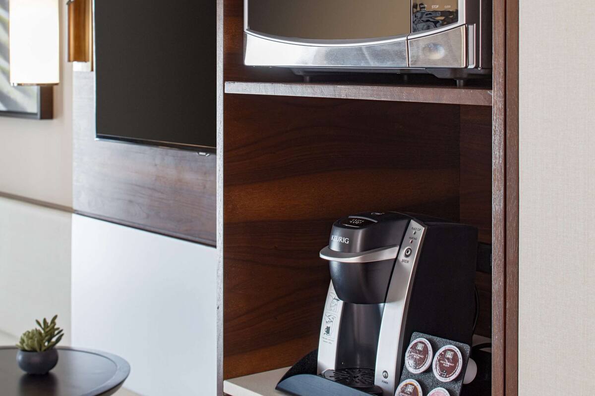 A compact kitchenette with a microwave, coffee maker, and a small table with a plant.