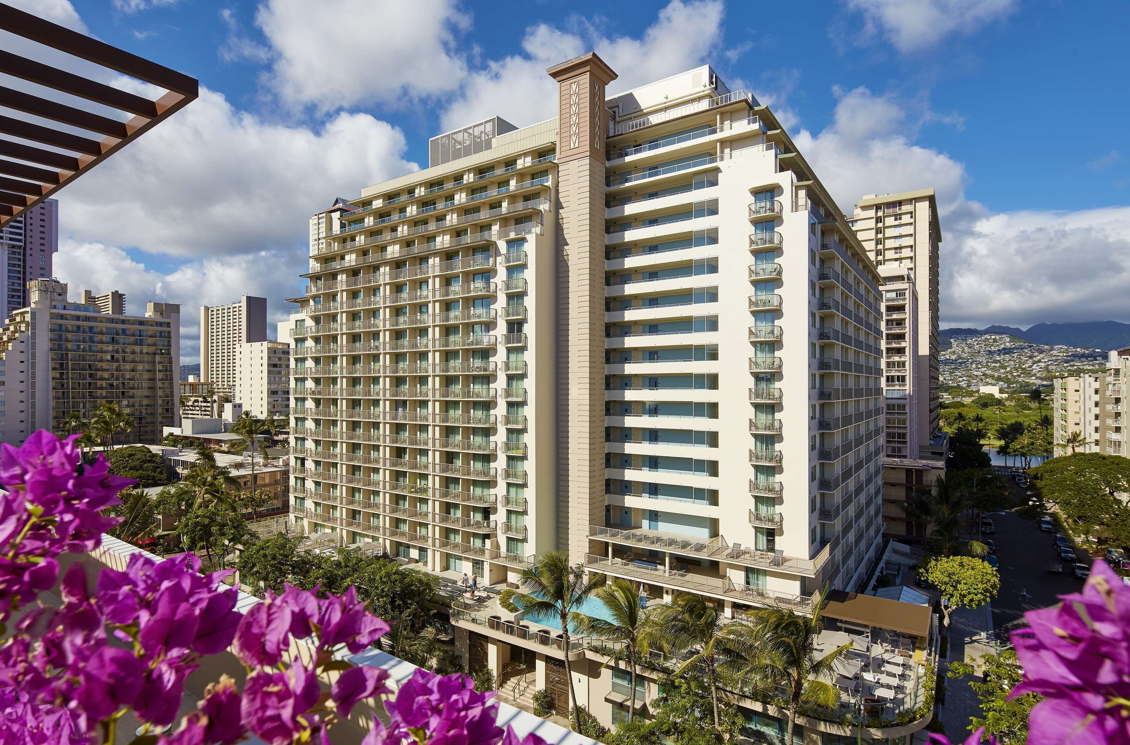 A high-rise hotel with multiple balconies, a pool area, and a view of the cityscape.