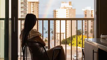 A person sitting on a balcony chair overlooking a cityscape with a rainbow.