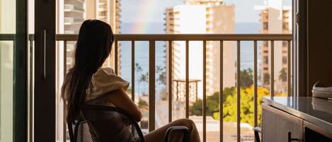 A person sitting on a balcony chair overlooking a cityscape with a rainbow.