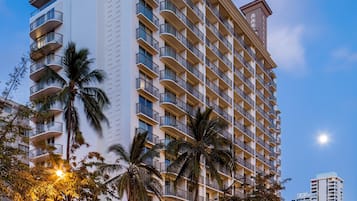 A high-rise hotel with multiple balconies, palm trees, and a storefront with illuminated signage.
