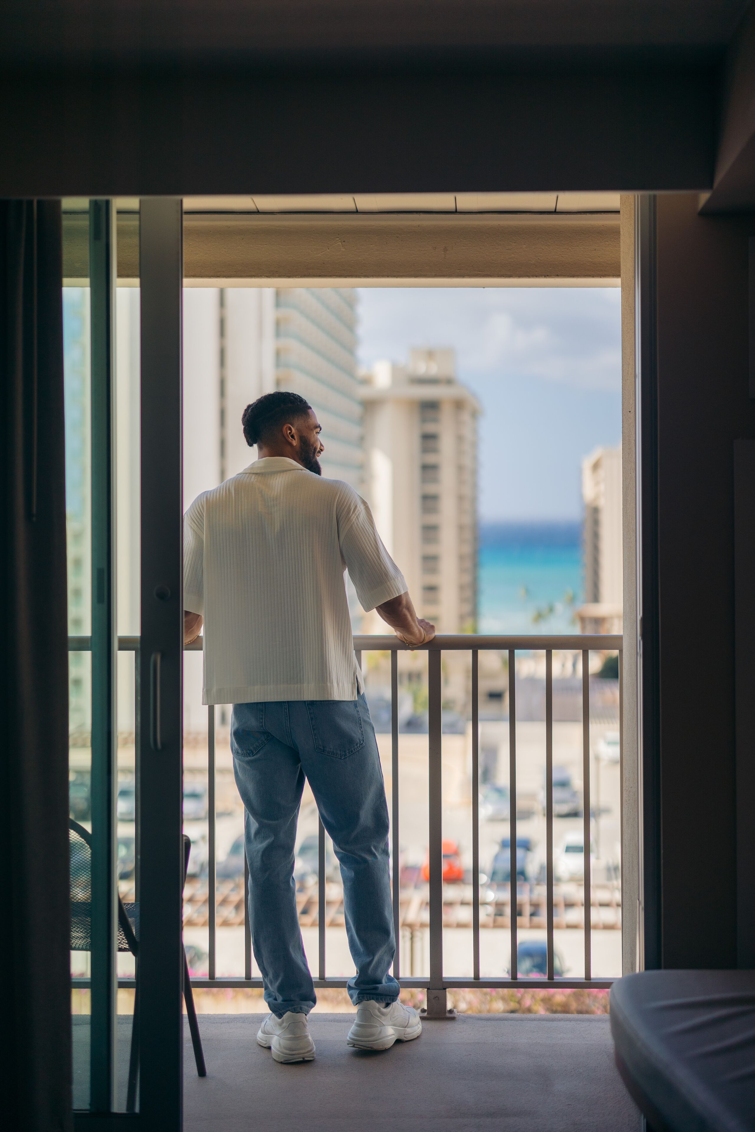 A man standing at a balcony with a view of a beach and buildings.