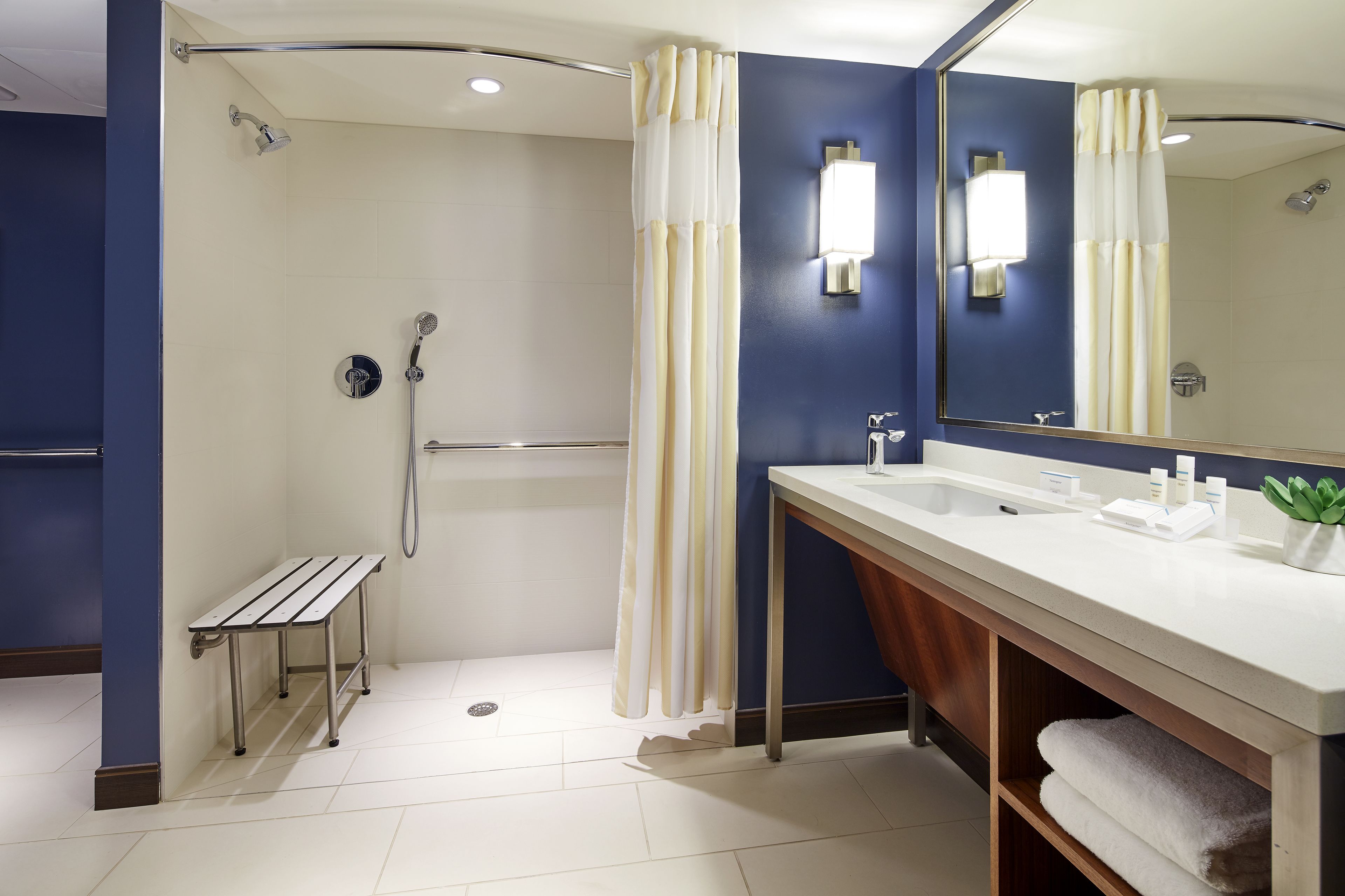 A modern bathroom with a shower, a bench, a sink, and a mirror.