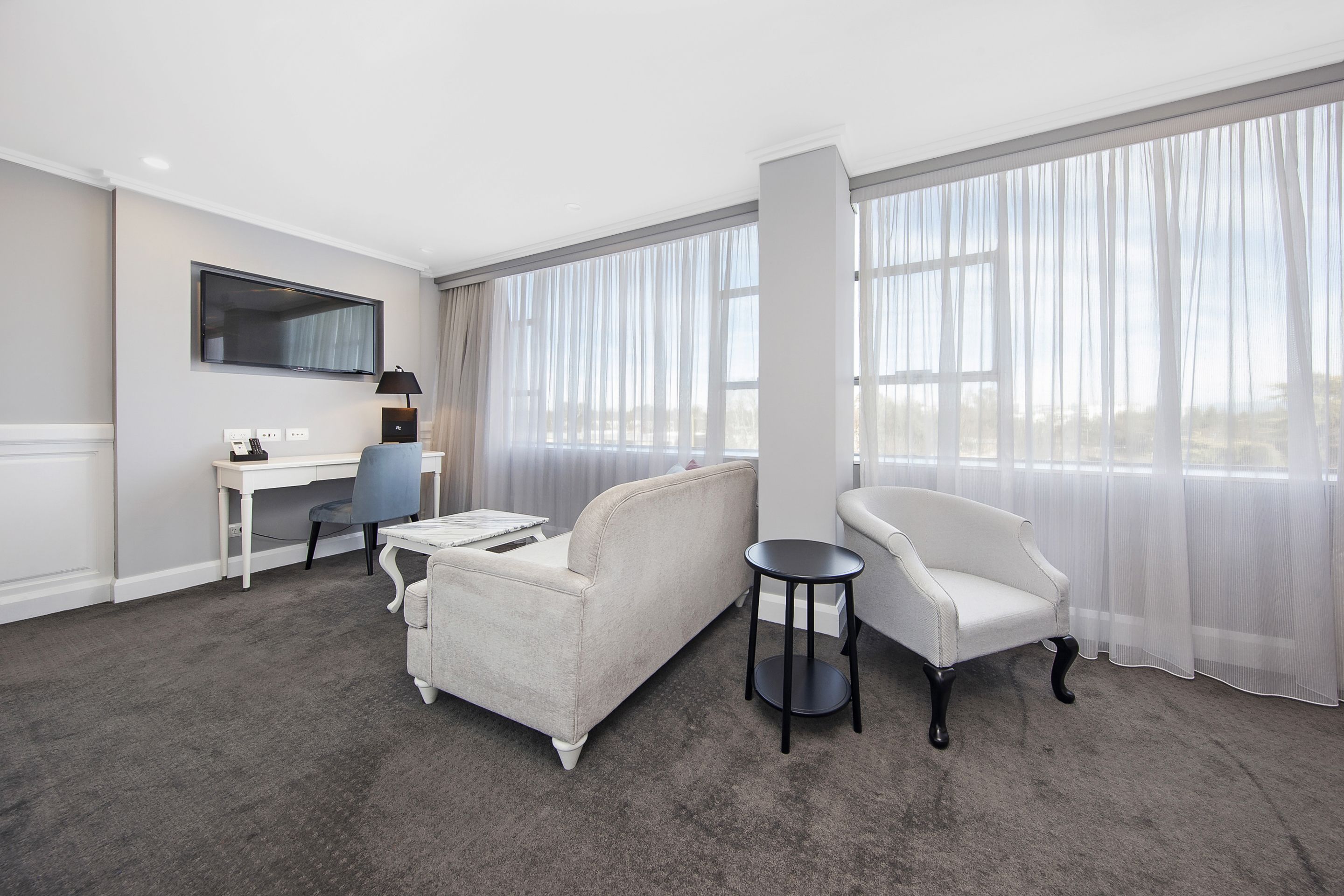 A hotel room with a large window, a sofa, a chair, a desk, and a television.