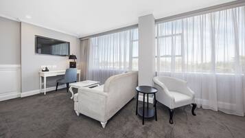 A hotel room with a large window, a sofa, a chair, a desk, and a television.