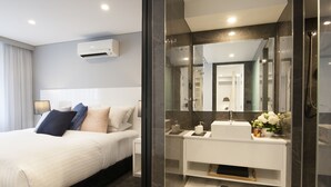 A modern hotel room with a large bed, a white bathroom with a glass shower enclosure, and a mounted air conditioner. - Canberra Rex Hotel (Braddon)