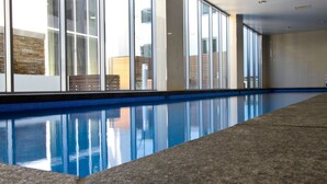 A swimming pool with clear blue water, surrounded by a stone wall and large windows. - Canberra Rex Hotel (Braddon)