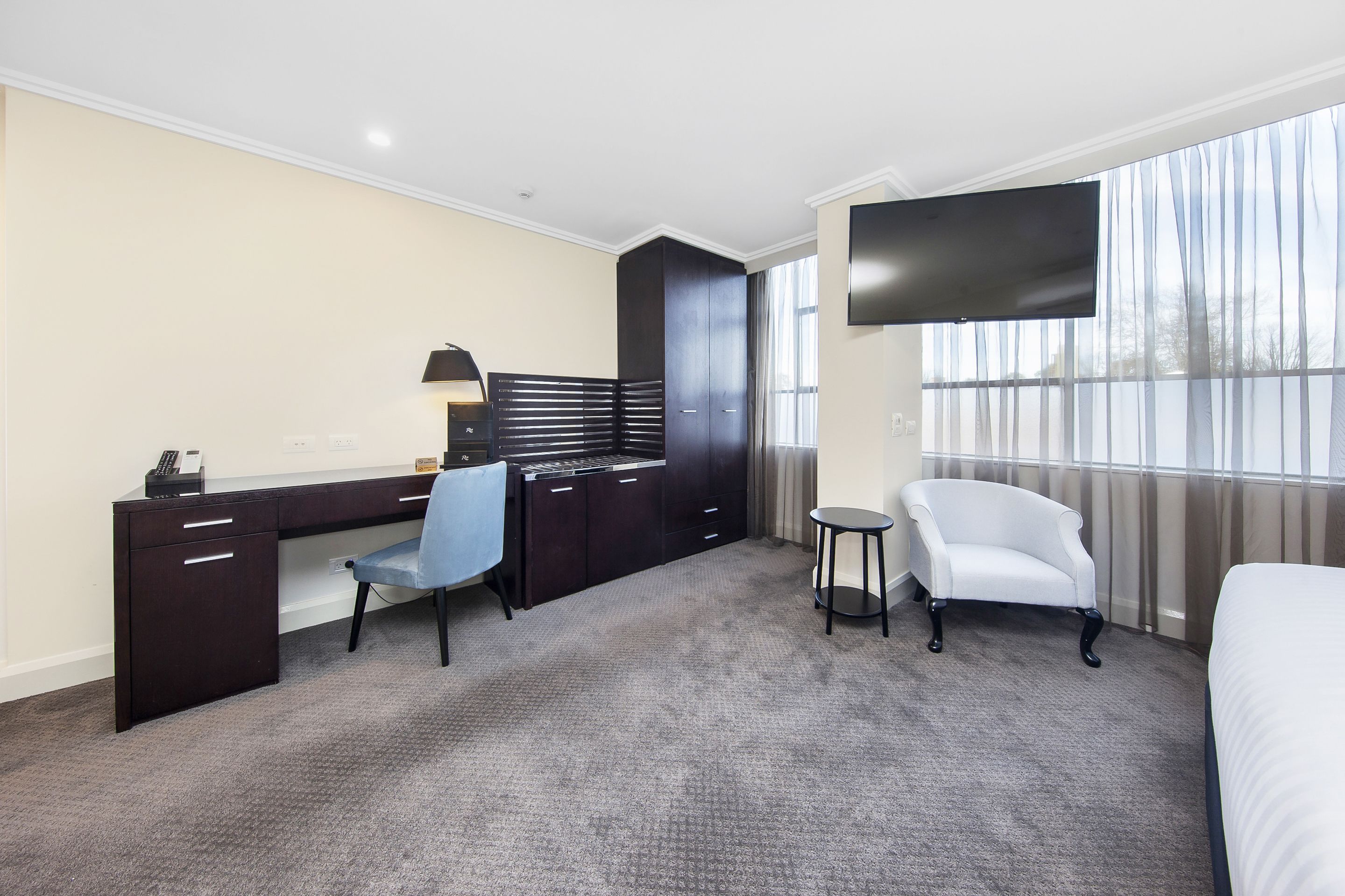A hotel room with a desk, chair, TV, and a bed.