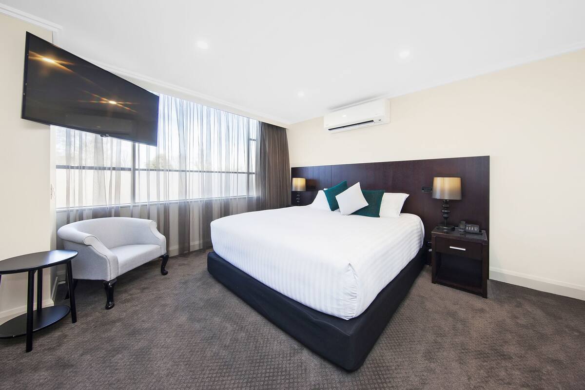 A hotel room with a large bed, a desk, a chair, a TV, and a window with curtains.