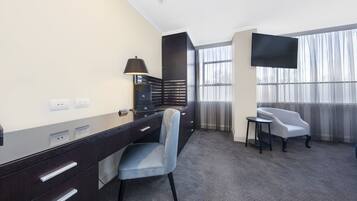 Ein Hotelzimmer mit Schreibtisch, Stuhl, Fernseher und großen Fenstern.