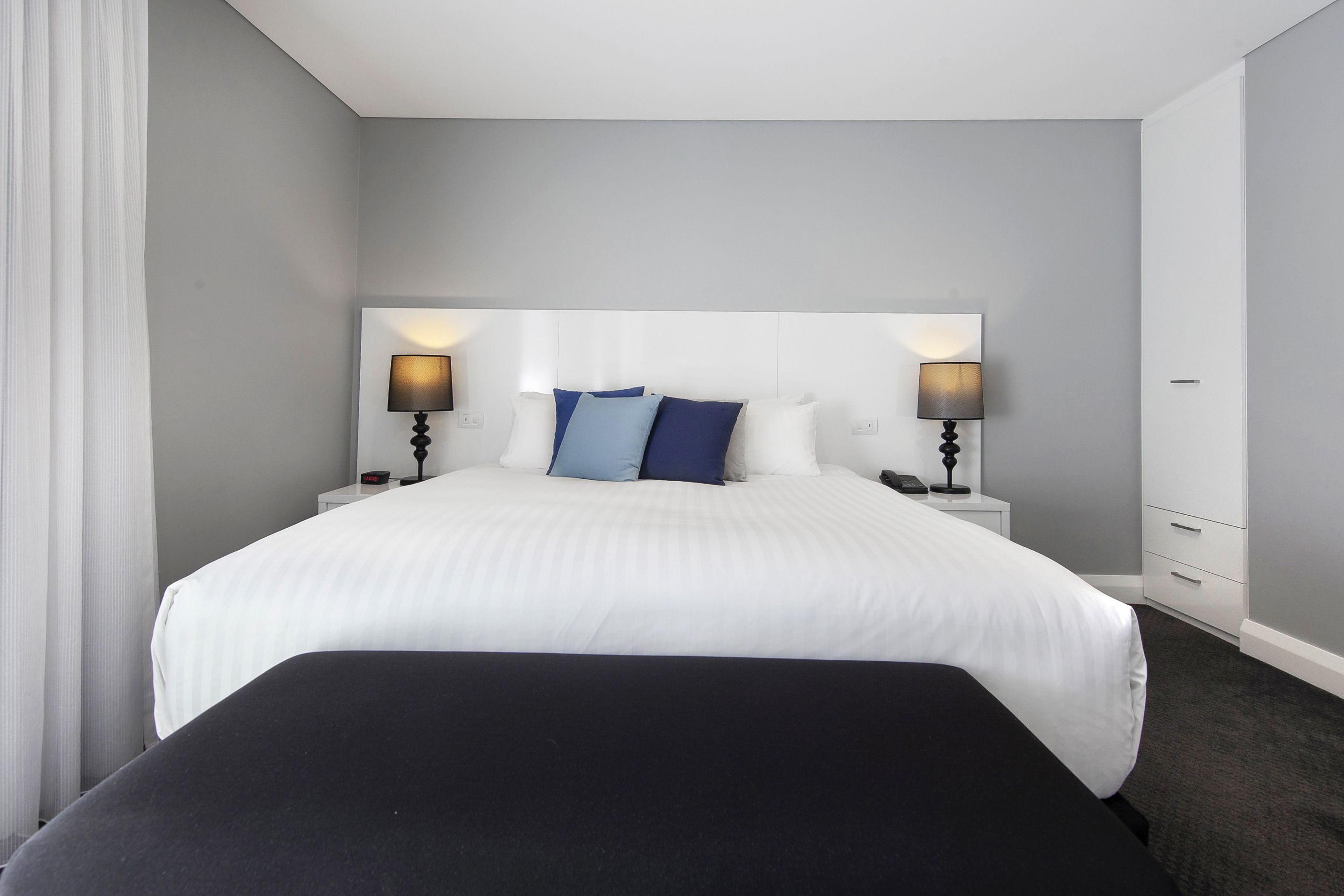 A hotel room with a large bed, two bedside tables with lamps, and a white headboard.