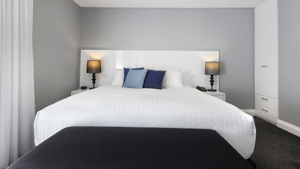 Una habitación de hotel con una cama grande, dos mesitas de noche con lámparas y un cabecero blanco.