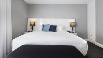 A hotel room with a large bed, two bedside tables with lamps, and a white headboard.