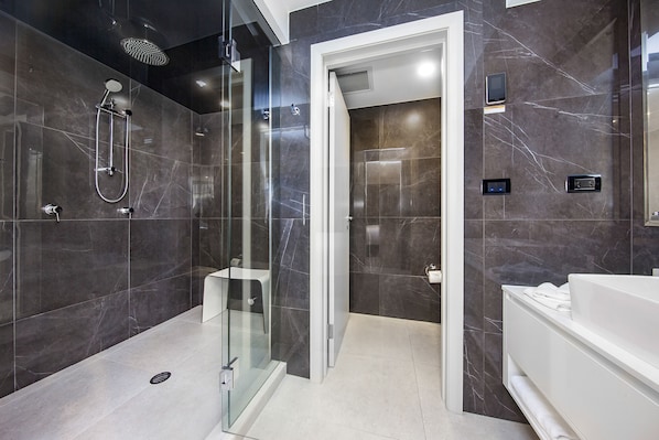 Un baño moderno con ducha envuelta en vidrio, tocador blanco y paredes de mármol.
