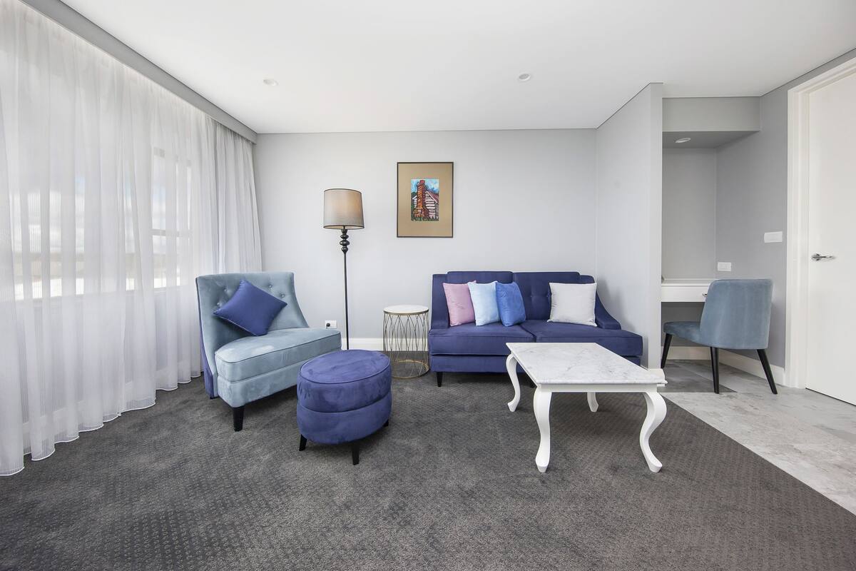A modern living room with a sofa, ottoman, and coffee table, a lamp, and a painting on the wall.
