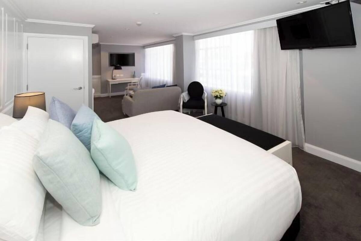 A hotel room with a large bed, a desk, a chair, a TV, and a small table with flowers.