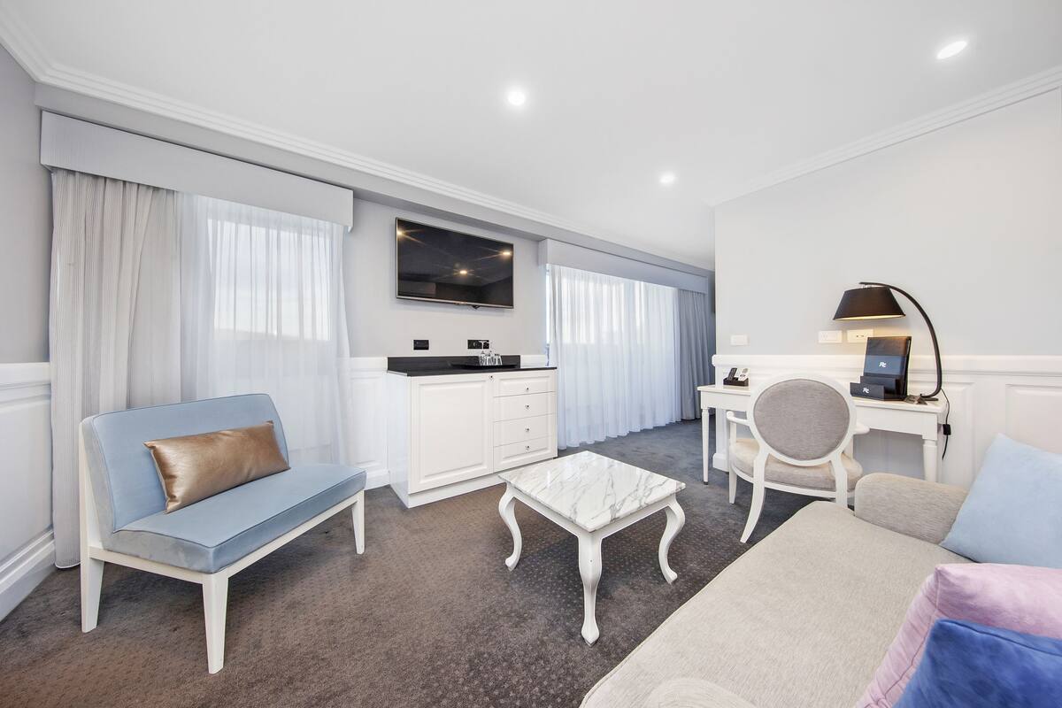 A modern hotel room with a sofa, a small table, a desk, and a chair.