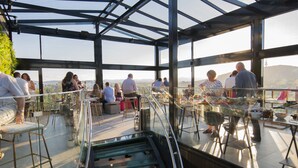 An indoor dining area with a glass railing, tables, and chairs, overlooking a scenic view. - Canberra Rex Hotel (Braddon)