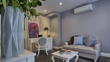 A modern living room with a grey sofa, a white desk, and a large plant.