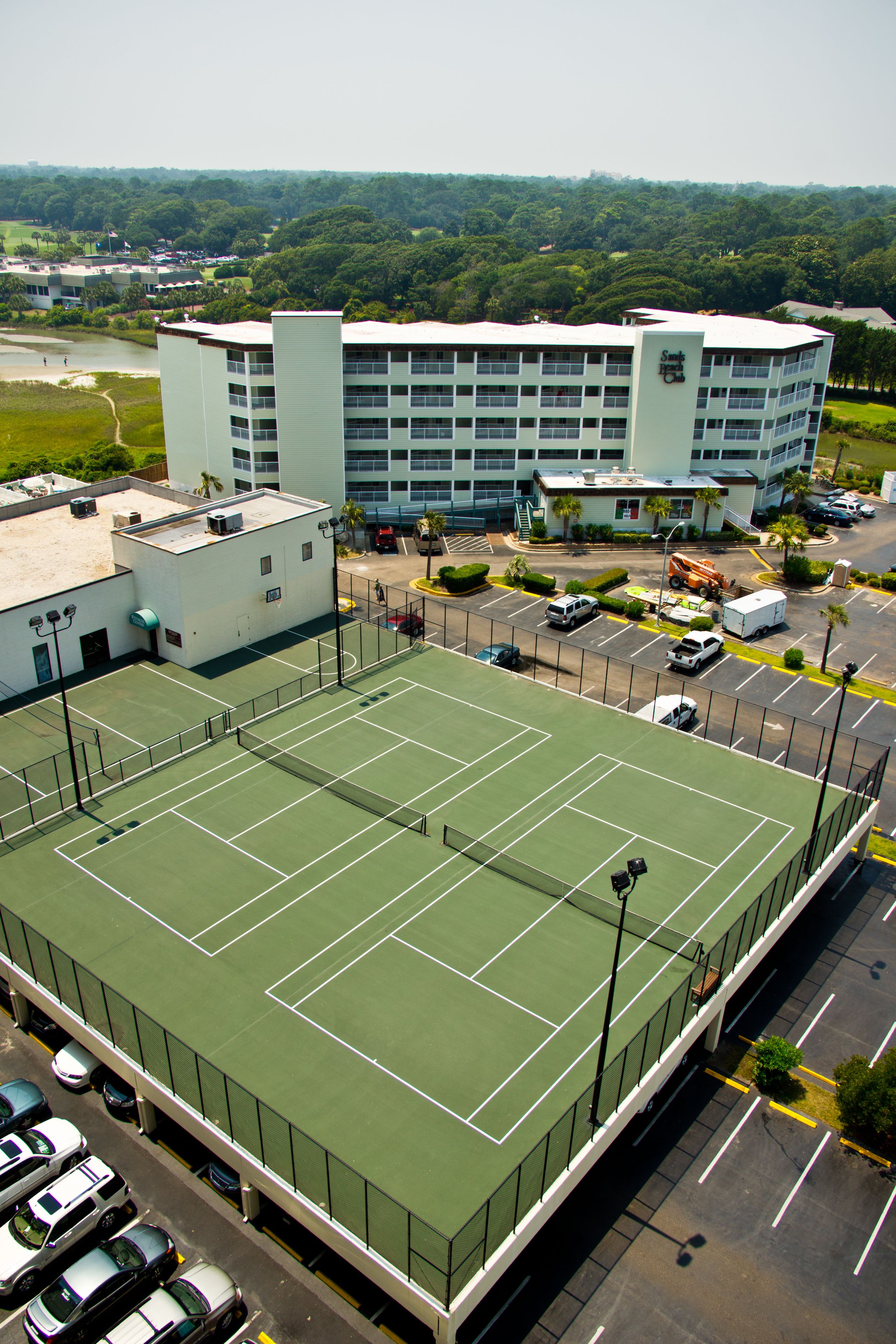 Ein mehrstöckiges Hotel mit Tennisplatz, Parkplatz und einem Golfplatz im Hintergrund.