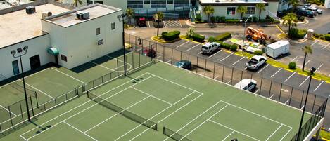 Ein mehrstöckiges Hotel mit Tennisplatz, Parkplatz und einem Golfplatz im Hintergrund.