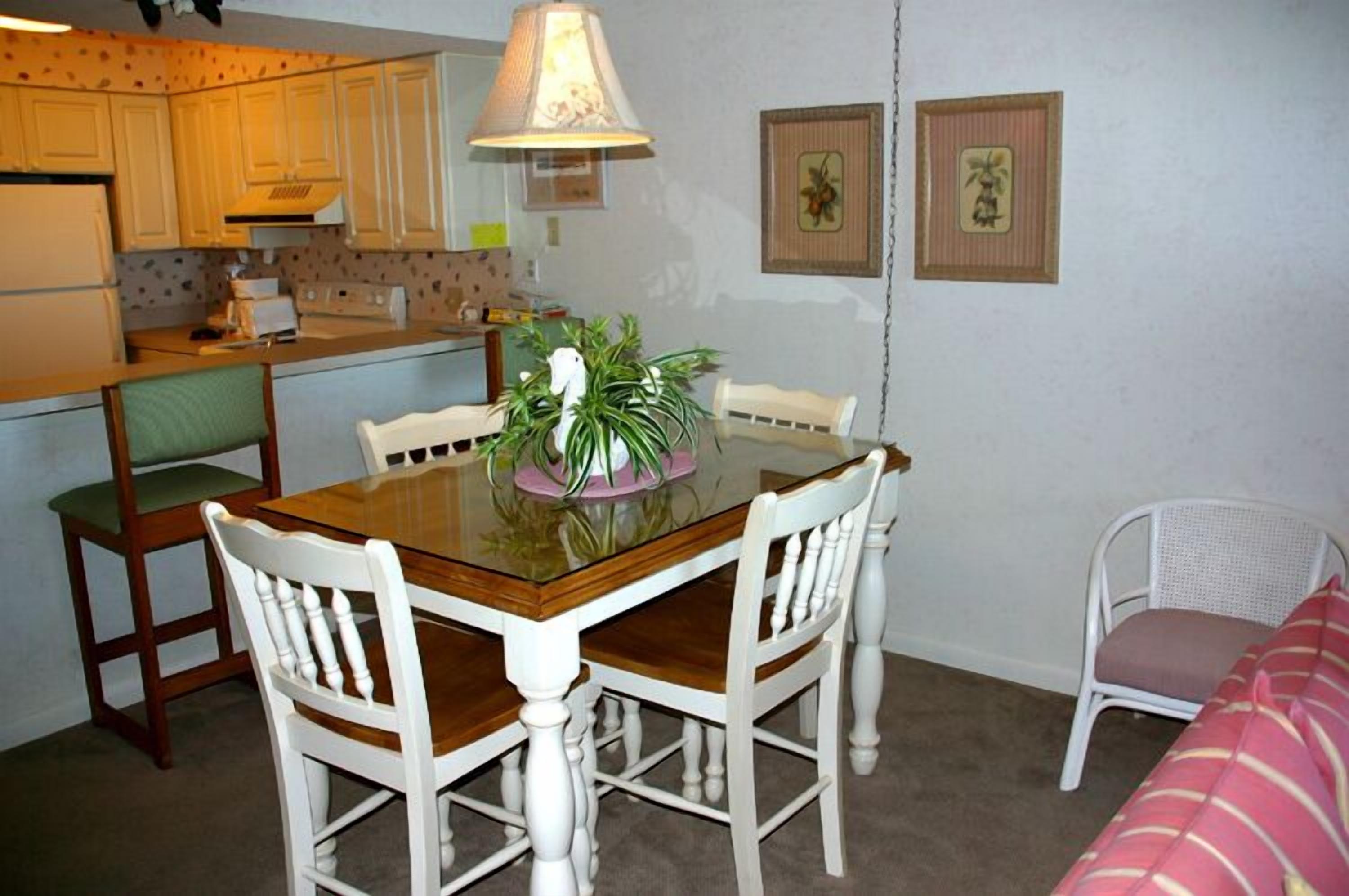 A compact kitchen with a dining table, chairs, and a hanging lamp.