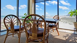 Ein Zimmer mit großen Fenstern und Meerblick, Korbmöbel, einem Tisch und Zimmerpflanzen.