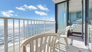 Ein Balkon mit Meerblick, ein Bett mit blauen und weißen Kissen und ein Bild an der Wand.