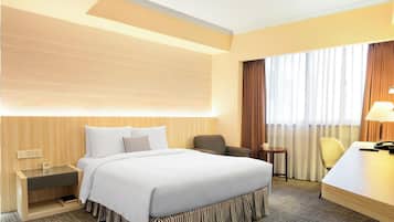 Ein Hotelzimmer mit Bett, Nachttisch, Lampe, Sessel und Schreibtisch mit Telefon.