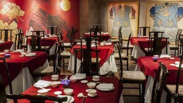 A restaurant with tables set for dining, featuring red tablecloths and traditional chairs.