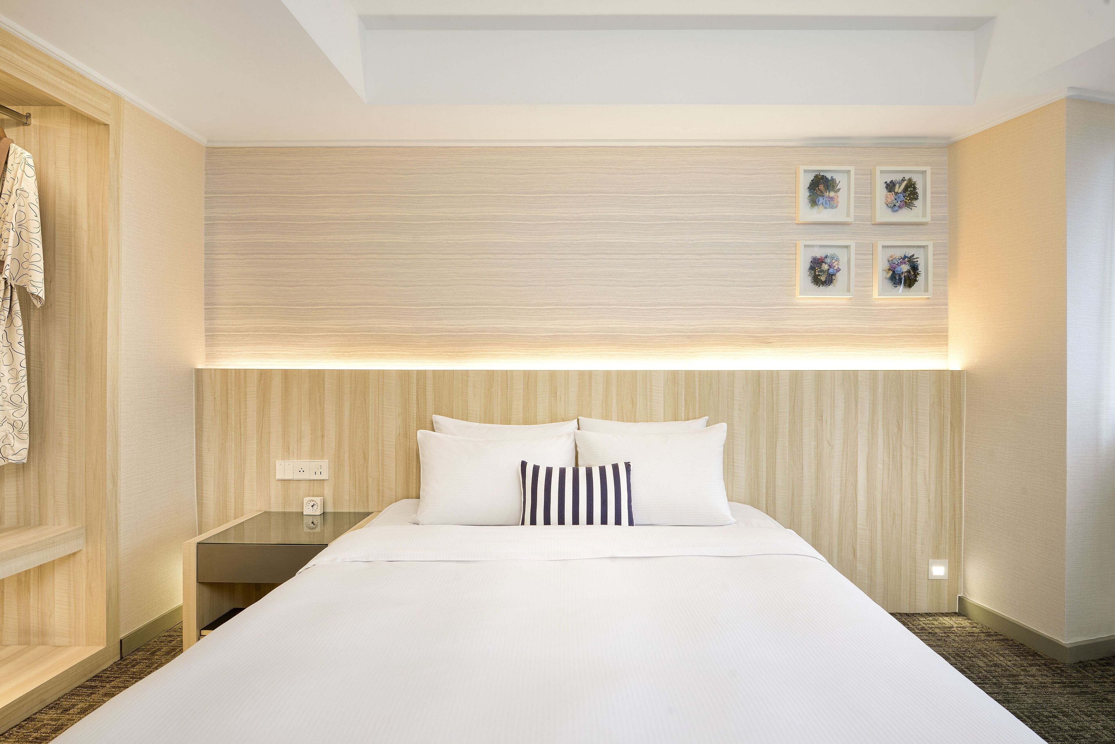 Una habitación de hotel con una cama grande, una mesita de noche, una lámpara de pared y un cuadro enmarcado sobre la cama.