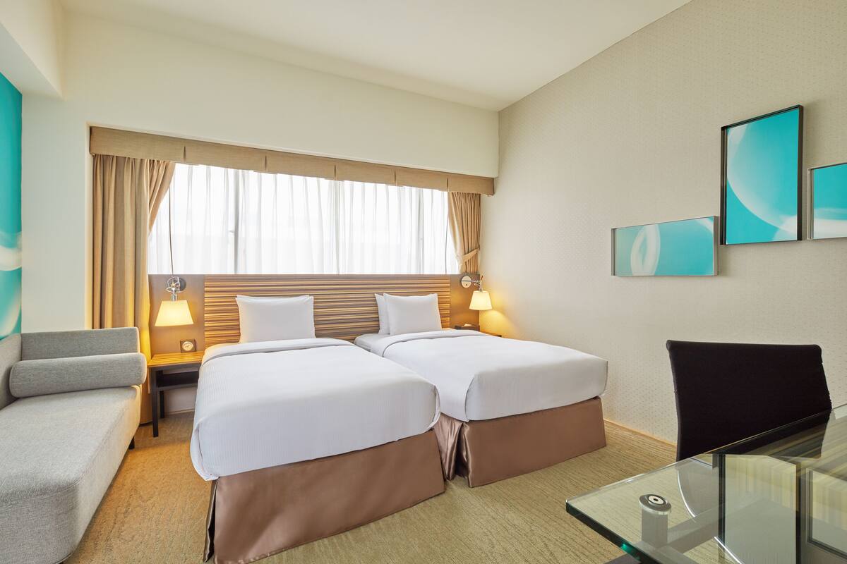 A hotel room with two beds, a sofa, a desk, and a chair.