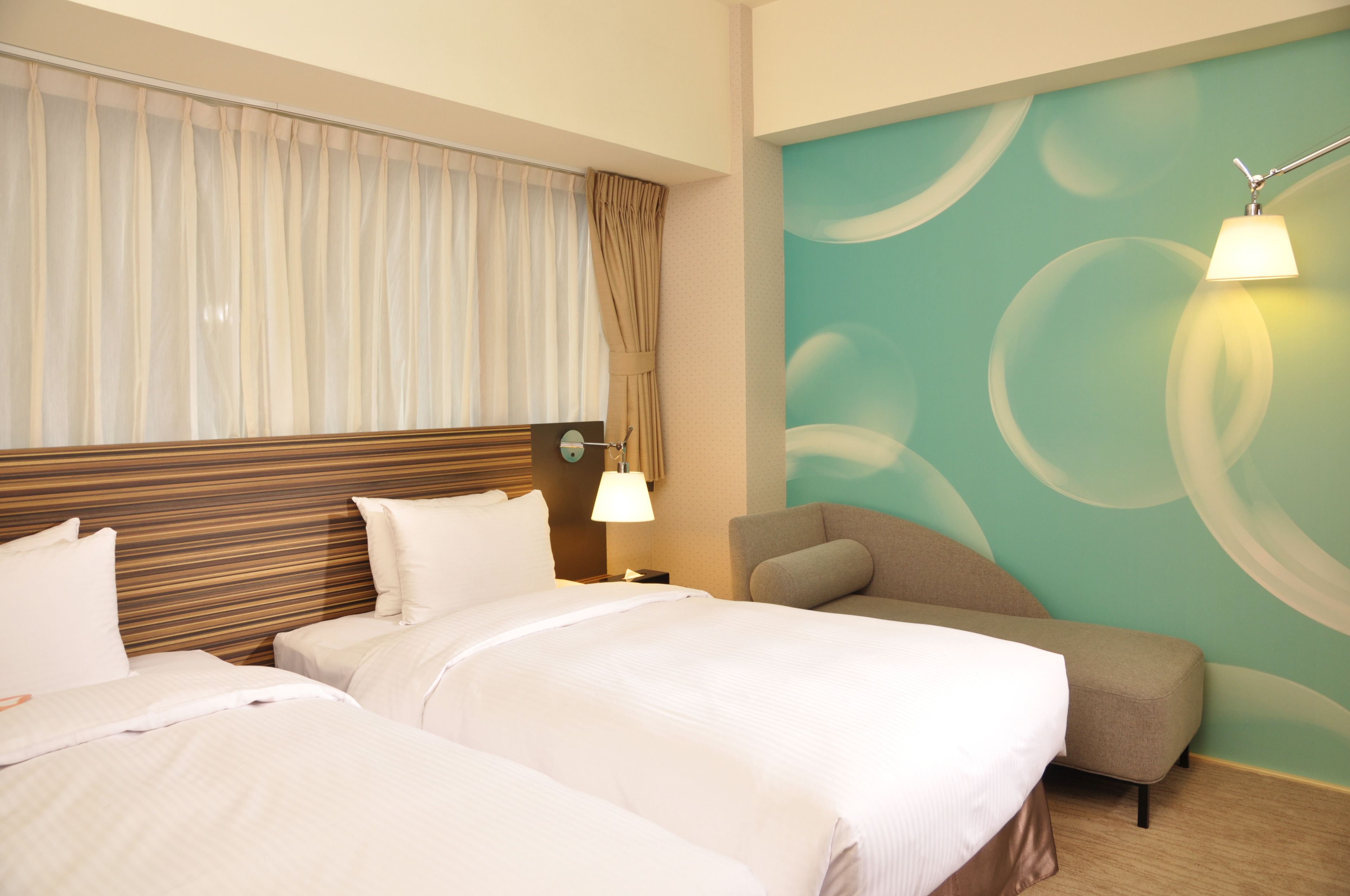 A hotel room with two beds, a sofa, a lamp, and a wall with a circular design.