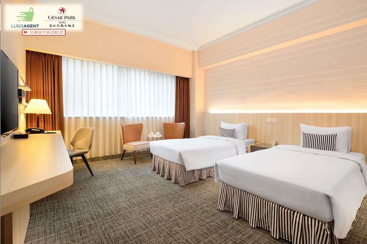 A hotel room with two beds, a desk, a chair, a TV, and a large window with curtains.