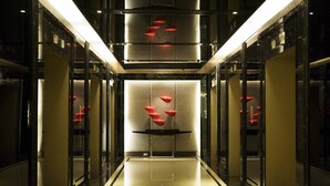 A modern hotel corridor with reflective floors, glass doors, and a central decorative element with red accents.