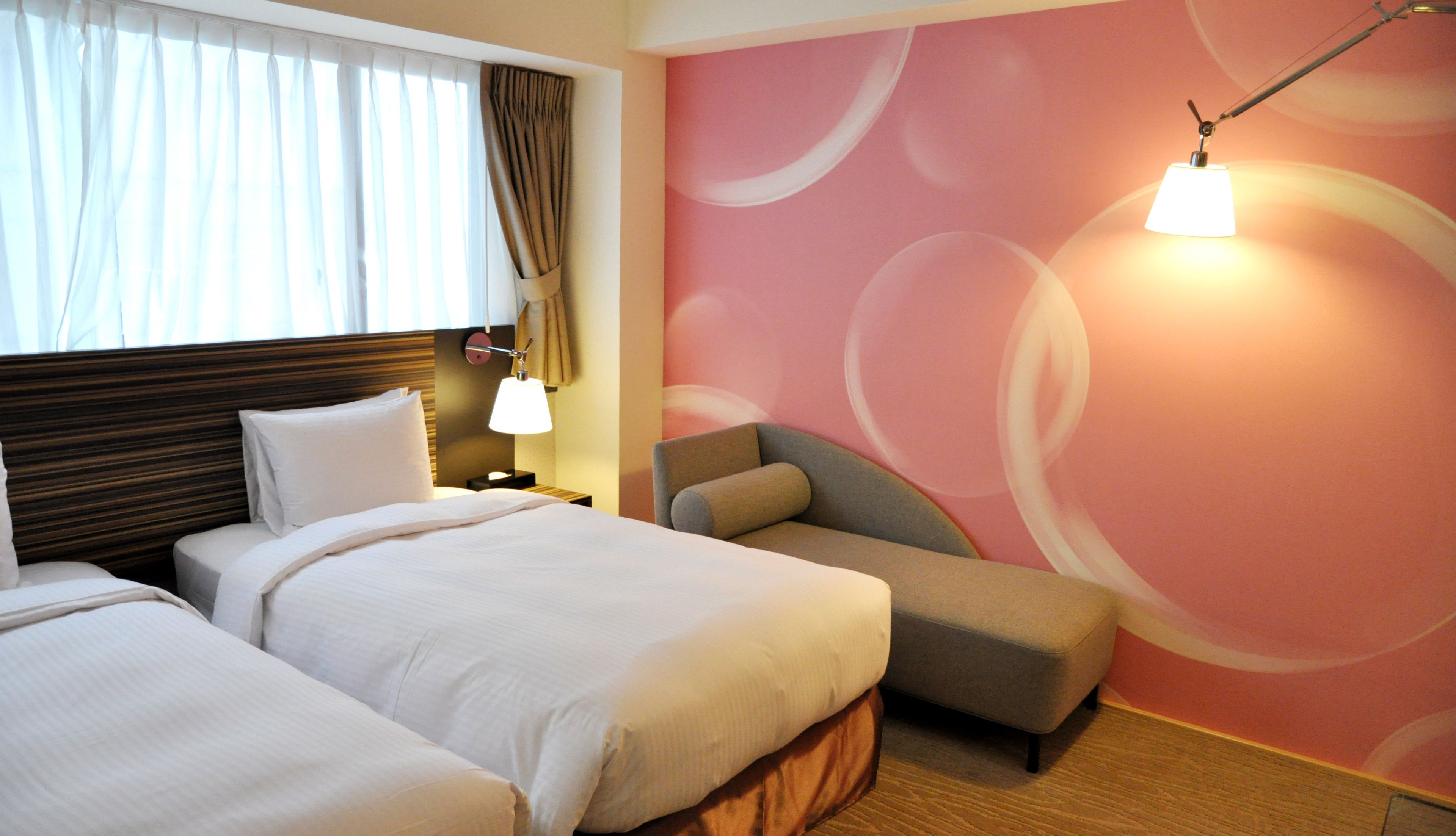 Quarto de hotel com duas camas, mesa de cabeceira, abajur e uma cadeira.