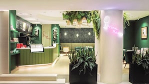 A modern bar area with a neon sign, green walls, and potted plants.