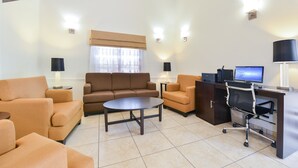 A modern living room with a brown sofa, a round coffee table, a desk with a computer, and a lamp. - Sleep Inn Sarasota North (Sarasota)