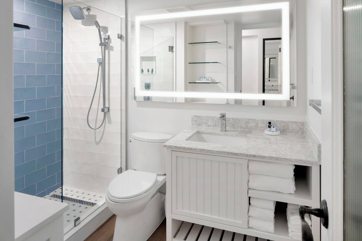 A modern bathroom with a shower, toilet, vanity, and a large mirror with built-in lighting.