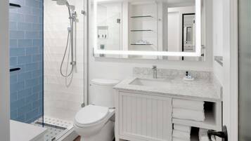 Un baño moderno con ducha, inodoro, tocador y un espejo grande con iluminación integrada.