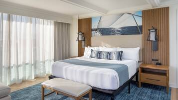 A hotel room with a large bed, a bench, a nightstand, and a painting of a sailboat on the wall.