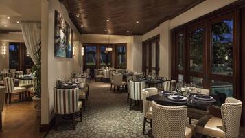 A restaurant with multiple tables and chairs, large windows, and a patterned carpet.