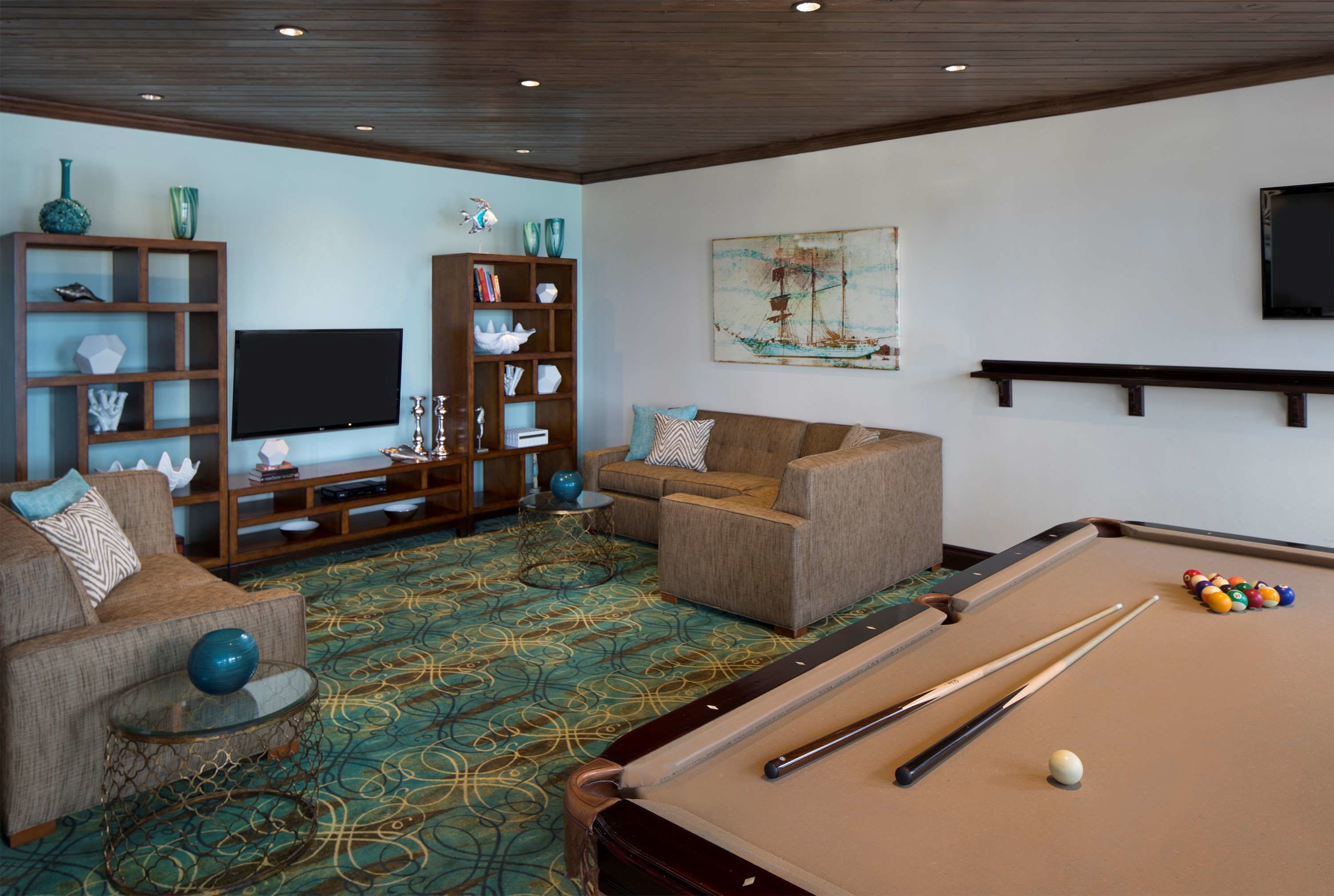 Une pièce équipée d’une table de billard, de canapés, d’un téléviseur et d’étagères où sont exposés des objets décoratifs.